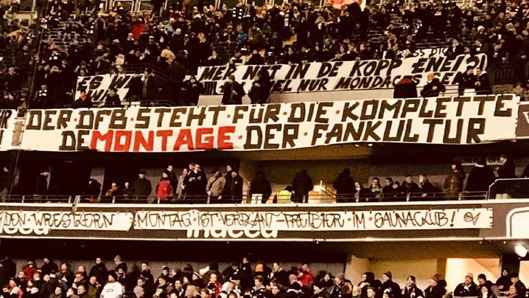 "ZDFzoom: Kick & Cash - Macht Geld den Fußball kaputt?": Blick auf eine Tribüne in einem Stadion. Viele Protestbanner sind zu sehen.