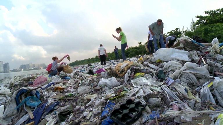 "planet e.: Der Plastik-Fluch - Wie wir unseren Planeten vermüllen": Ein beliebiger Plastikmüllberg. Nur ein winziger Teil von dem, was angespült wird. Mehrere Personen laufen auf dem Müllberg herum.