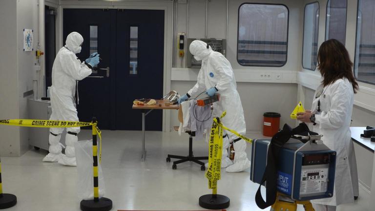 "Kampf gegen Atomschmuggler: Terrorgefahr durch schmutzige Bomben": Zwei Männer und Frauen in Schutzanzügen im Trainingscenter für nukleare Sicherheit in Karlsruhe