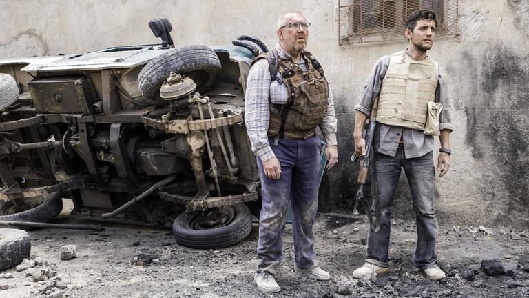 "Für meine Tochter": Benno Winkler (Dietmar Bär) und sein Fahrer Ilkay (Adam Bay) stehen auf einer Straße, der man die Spuren des Krieges deutlich ansieht: Granateinschläge haben den Boden aufgewühlt, hinter den beiden liegt ein ausgebranntes Auto auf der Seite.  Beide sind mit Splitterschutzwesten ausgerüstet, Ilkay hält ein AK47-Kalaschnikow- Sturmgewehr in den Händen. Beide sehen angespannt aus.