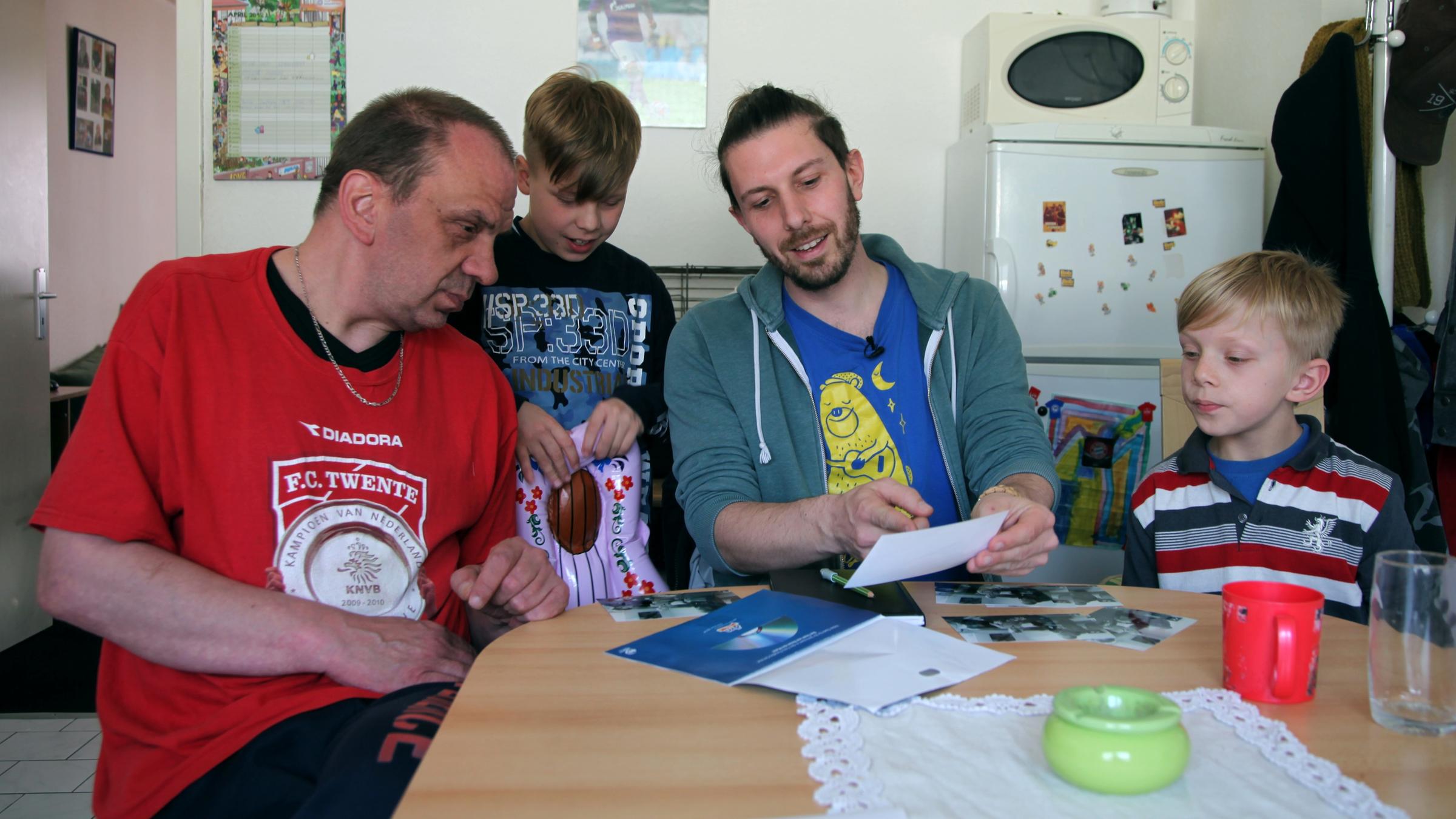 ""37°: Die Schicksalswender - Unterwegs mit Sozialarbeitern": Pablo M. sitzt mit einem Vater und zwei Söhnen in deren Küche, sie schauen sich Fotos an.