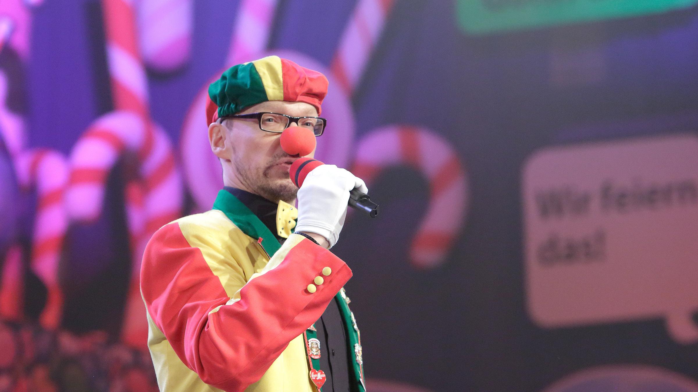 "Kölle Alaaf - Die Mädchensitzung": Redner "Dä Tuppes vum Land" steht auf der Bühne mit einem Mikrofon in der Hand.