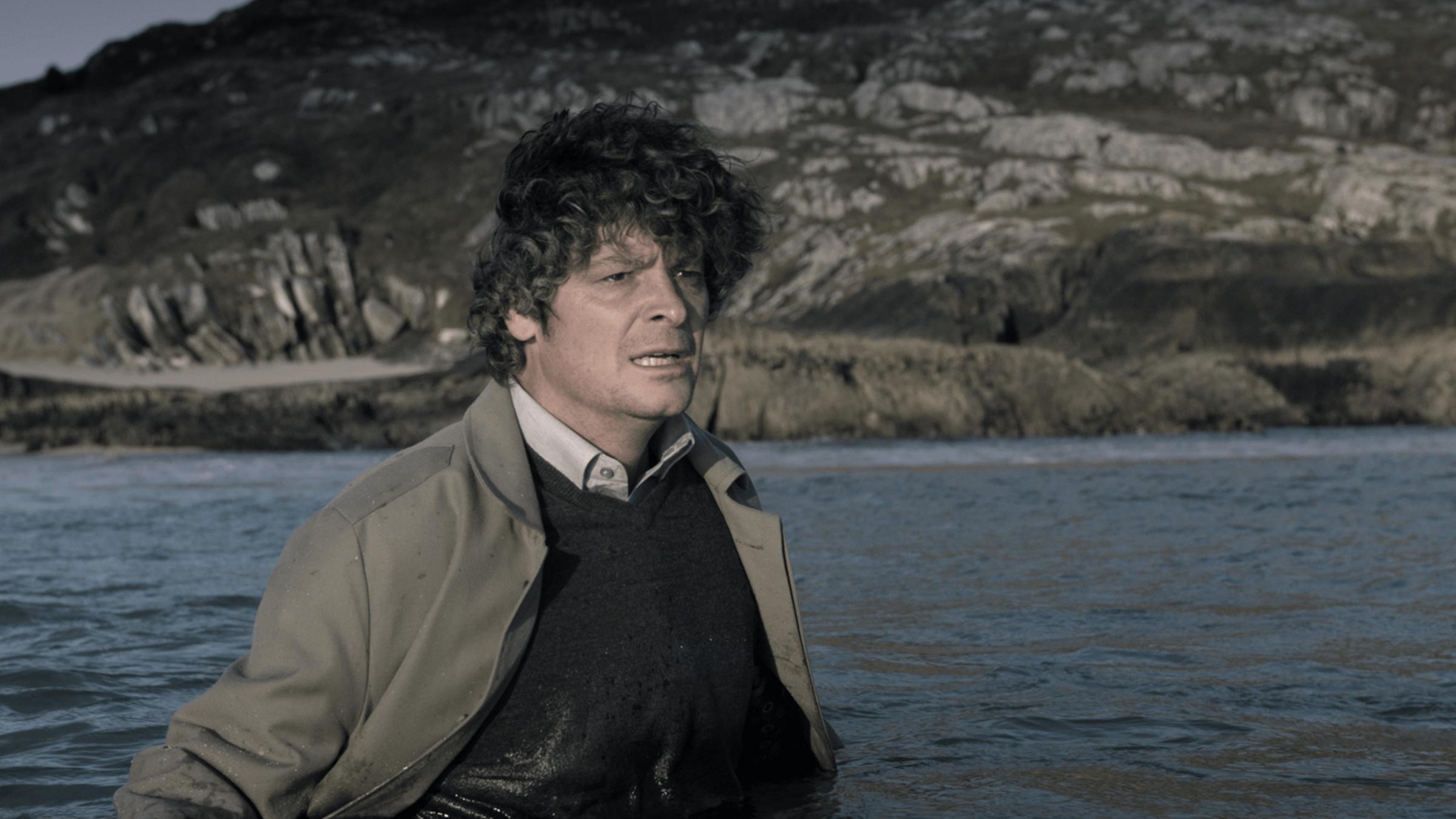 "Inspektor Jury - Der Tod des Harlekins": Inspektor Jury (Fritz Karl) steht voll angezogen bis zur Brust im Meer, im Hintergrund die felsige Küste.