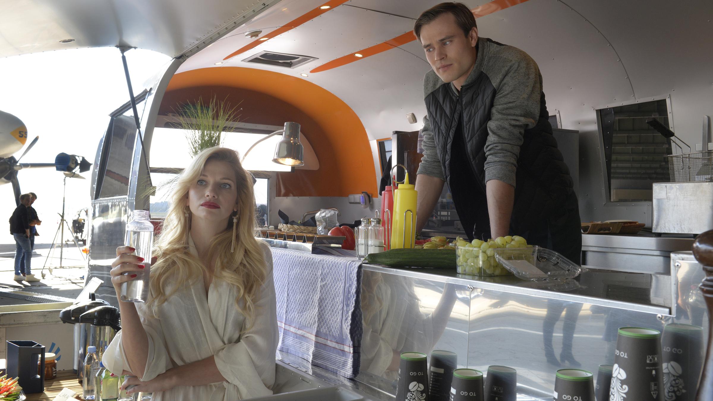  "Ein starkes Team – Preis der Schönheit": Leonie Seiters (Amelie Otto) steht mit einer Wasserflasche vor Patrick Heise (Christopher Reinhardt) in dessen Cateringwagen. Sie schaut ins Leere, während Patrick sie beobachtet.