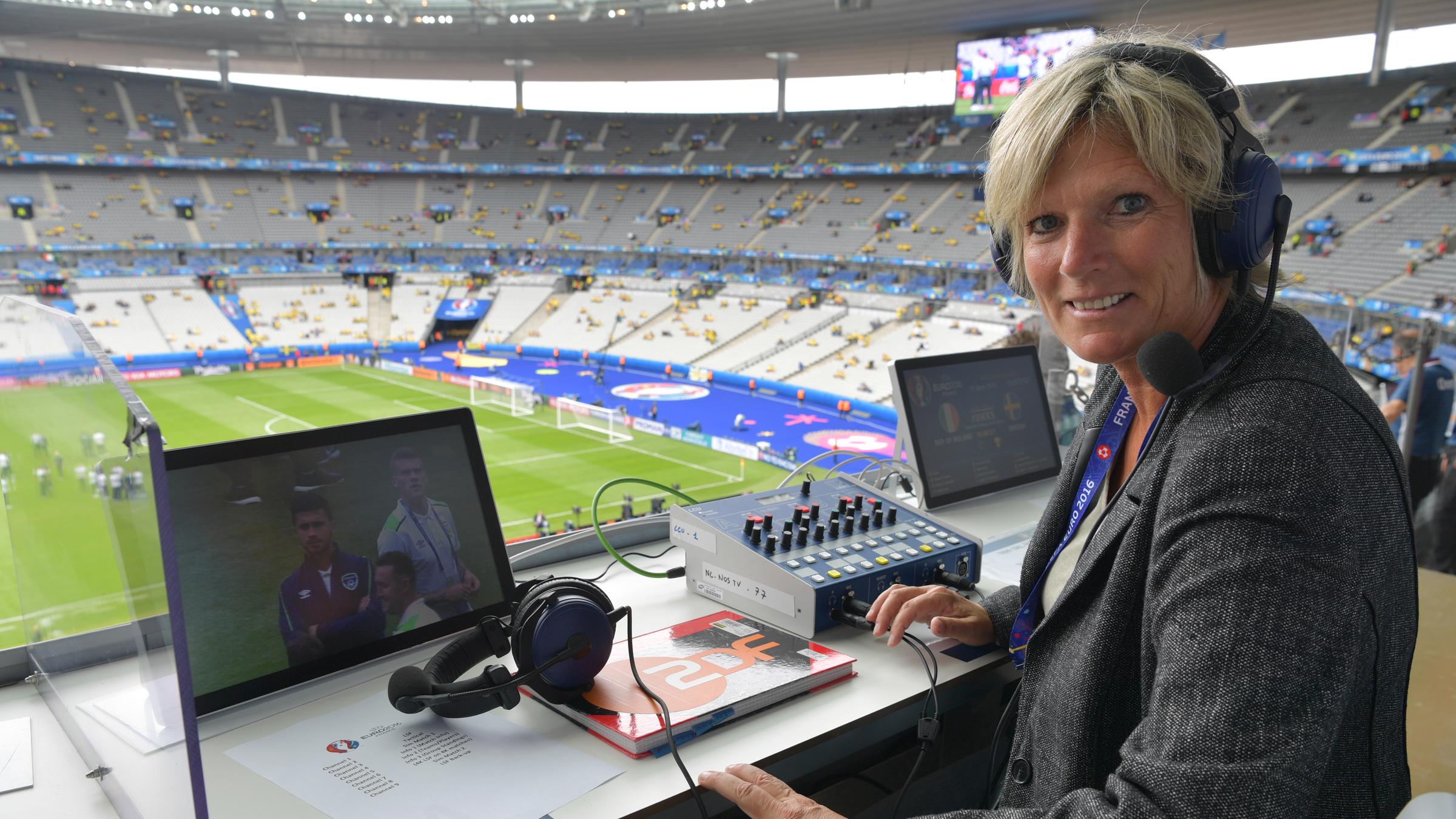 Claudia Neumann mit Kopfhörern an ihrem Arbeitsplatz sitzend im Stadion