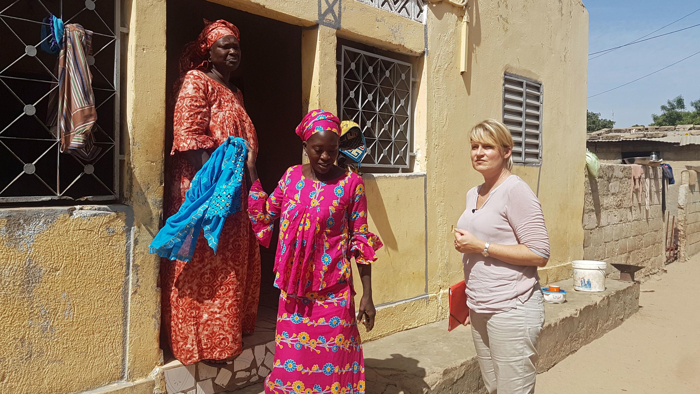 "ZDFzoom: Der Wahnsinn mit dem Weizen": Die Autorin Katarina Schickling tritt mit zwei senegalesischen Frauen aus einem Haus.