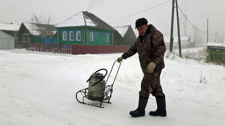 "10.000 Kilometer Russland (1)": In einem verschneiten russischen Dorf transportiert Sergej eine Wasserkanne auf dem Schlitten.