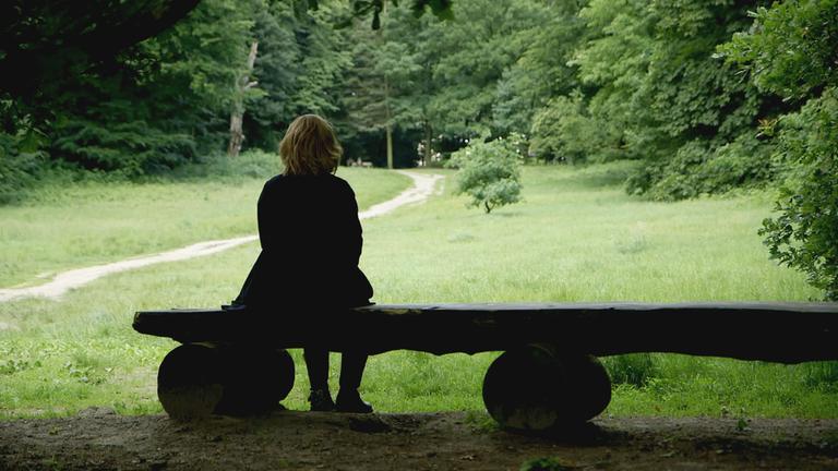 "37°: Das dunkle Geheimnis - Missbrauch in der Familie": In einer Waldlichtung sitzt Johanna auf einer Holzbank.