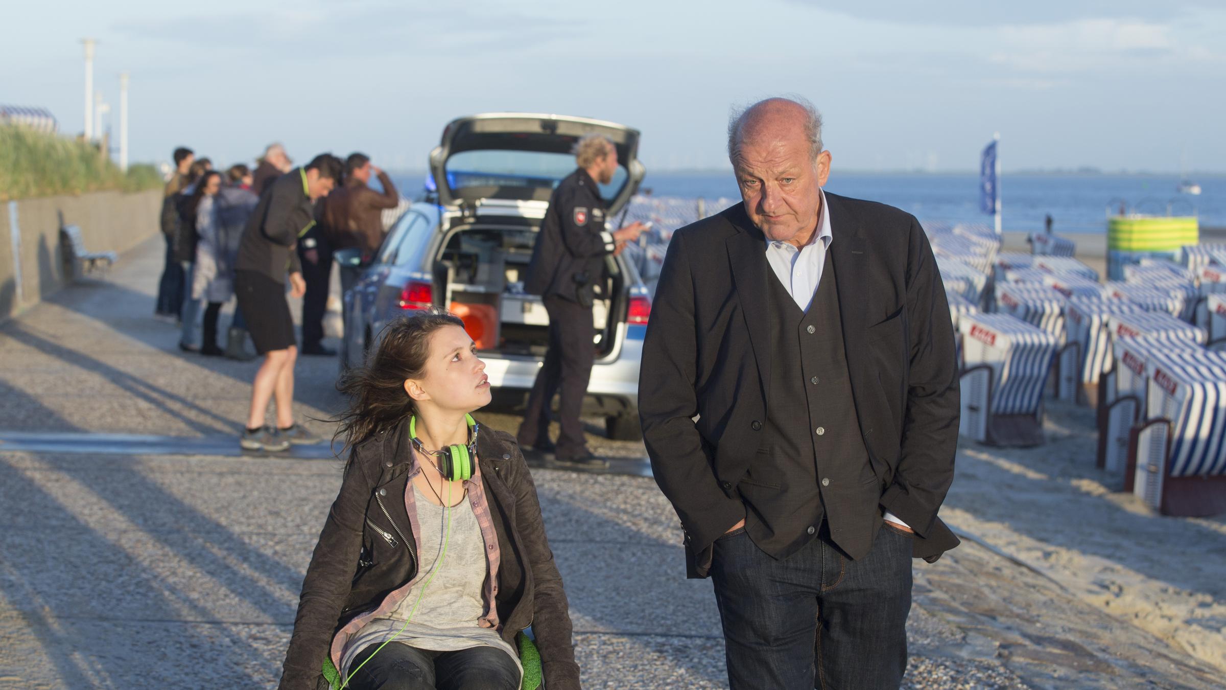 "Wilsberg - Morderney": Merle (Janina Fautz) fährt in ihrem Rollstuhl neben Wilsberg (Leonard Lansink) an der Strandpromenade entlang. Das Mädchen schaut ihn an, er hat die Hände in den Hosentaschen und sieht nach vorne.