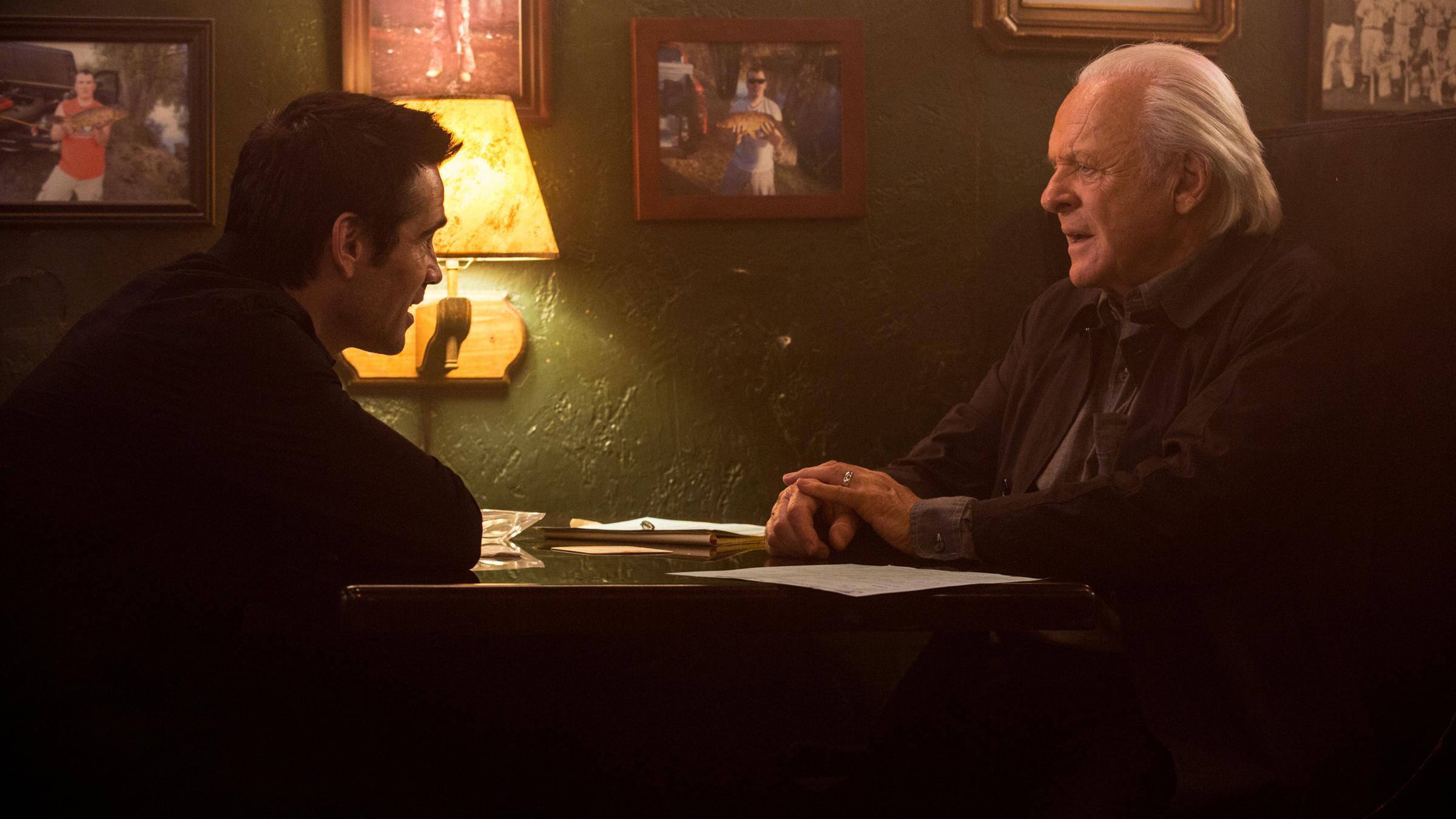 "Die Vorsehung": Charles Ambrose (Colin Farrell) und Dr. John Clancy (Anthony Hopkins) sitzen sich an einem Tisch gegenüber und unterhalten sich. An der Wand hinter ihnen hängen zahlreiche Bilder, eine Wandleuchte erhellt die Szenerie.