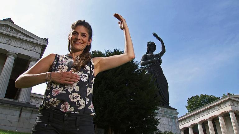 "aspekte"-Moderatorin Katty Salié imitiert die stolze Pose der bayerischen Schutzpatronin „Bavaria“ vor deren imposanten Statue an der Münchner Theresienwiese.