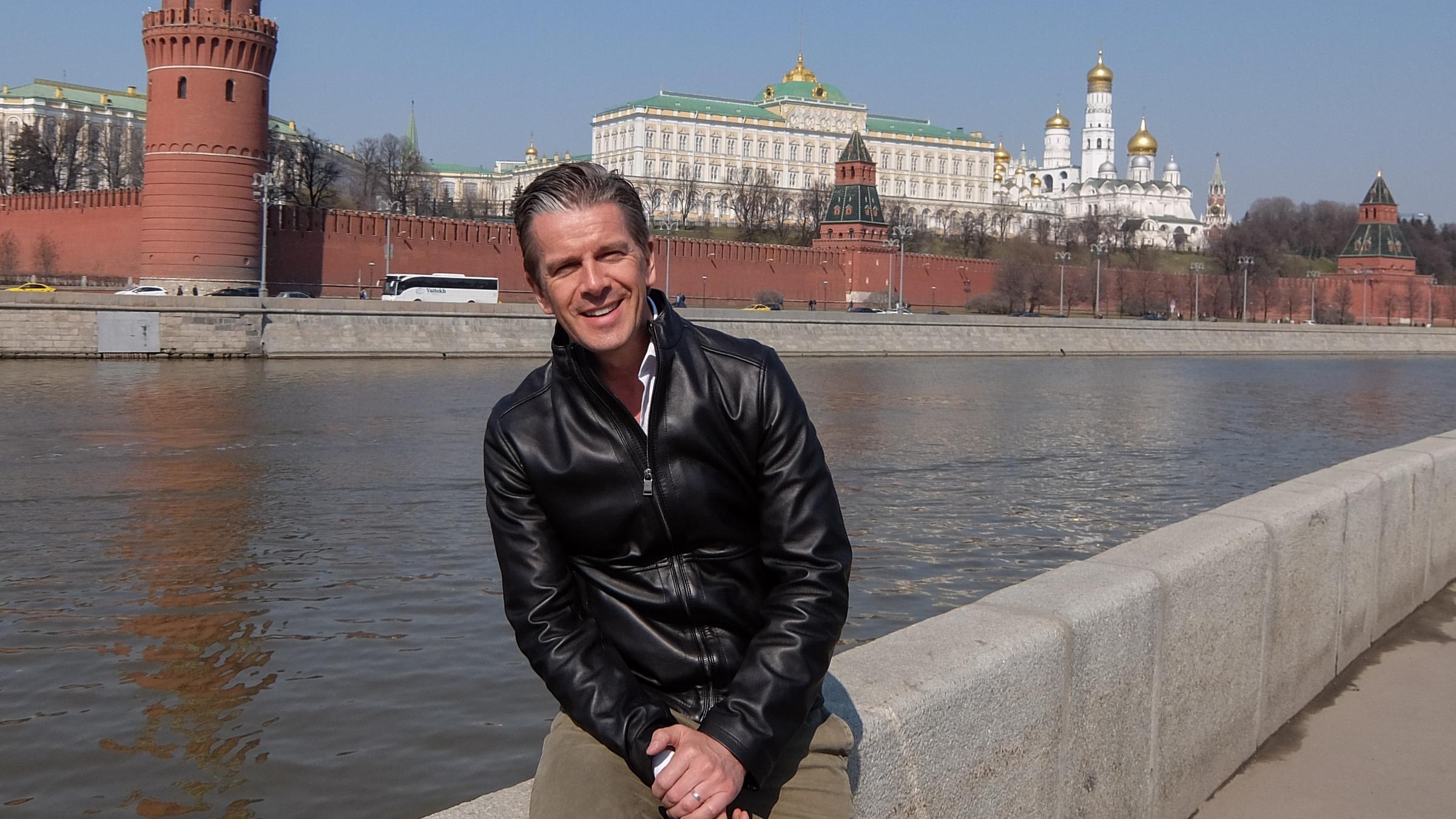 "Markus Lanz - Russland!": Markus Lanz sitzt auf einer Ufermauer und lacht in die Kamera. Im Hintergrund ist der Kreml in Moskau zu sehen.