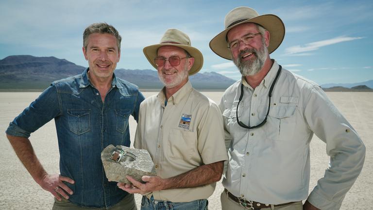 "Terra X: Rätselhafte Phänomene - Verschwundene Inseln und wandernde Steine": Dirk Steffens, Jim und Richard Norris stehen in einer Wüstenlandschaft nebeneinander und lachen in die Kamera. Jim hält einen präparierten Stein in  den Händen.