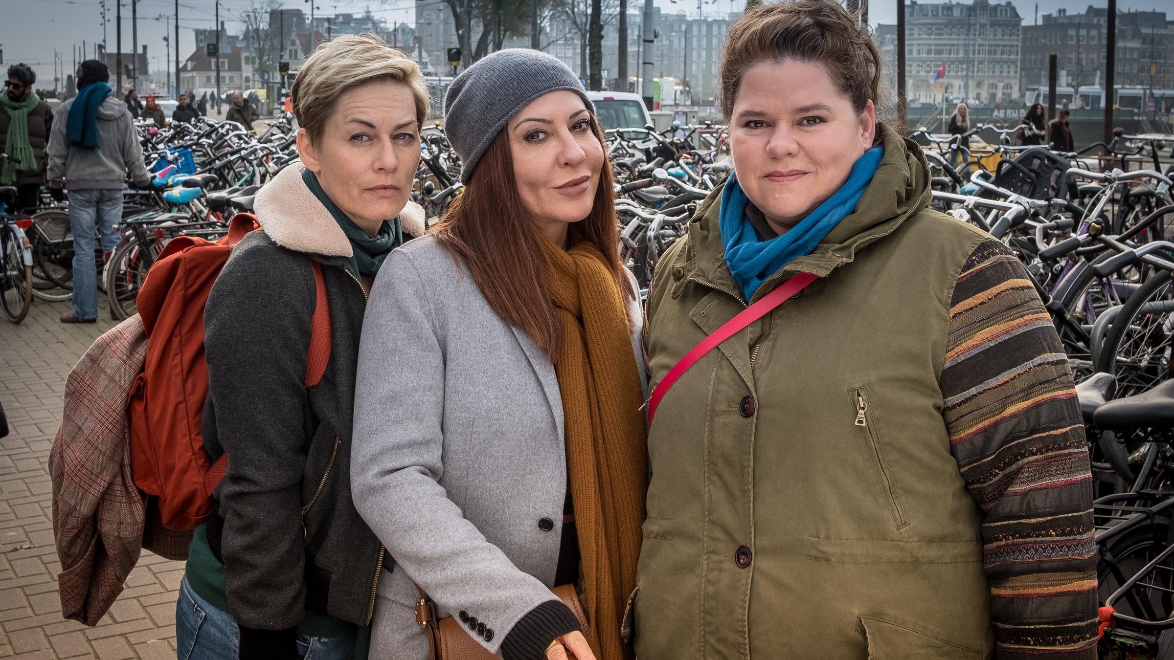 "Doppelzimmer für drei": Hilde (Gesine Cukrowski), Anne (Simone Thomalla) und Conny (Nadine Wrietz) stehen am Amsterdamer Hauptbahnhof und schauen in die Kamera. Im Hintergrund sind viele Fahrräder zu sehen.