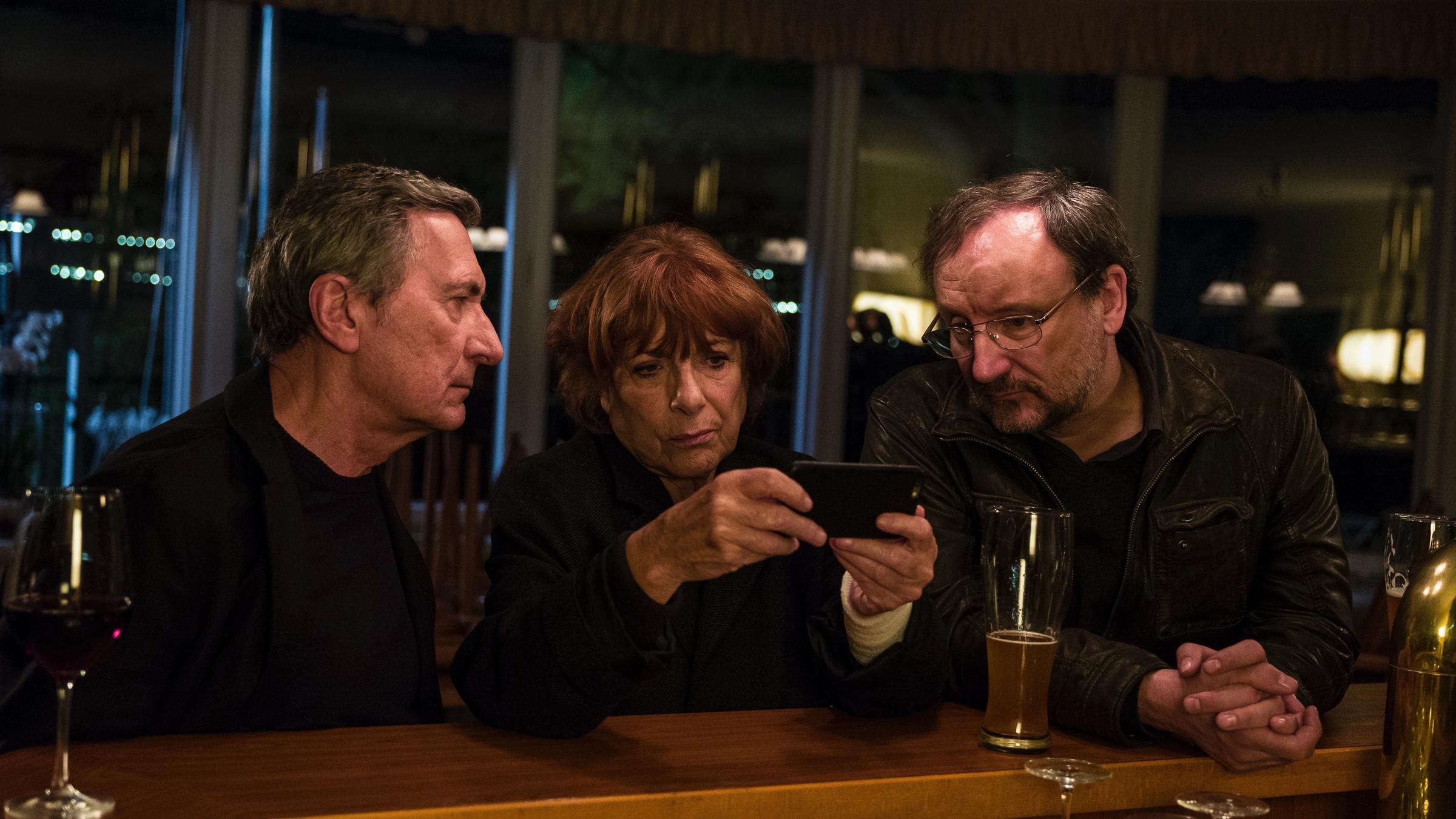 "Bella Block - Am Abgrund": Bella Block (Hannelore Hoger, m.), Schnaak (Rainer Bock, r.) und Simon Abendroth ( Rudolf Kowalski, l.) schauen sich am Tresen einer Bar auf einem Handy Fotos an.