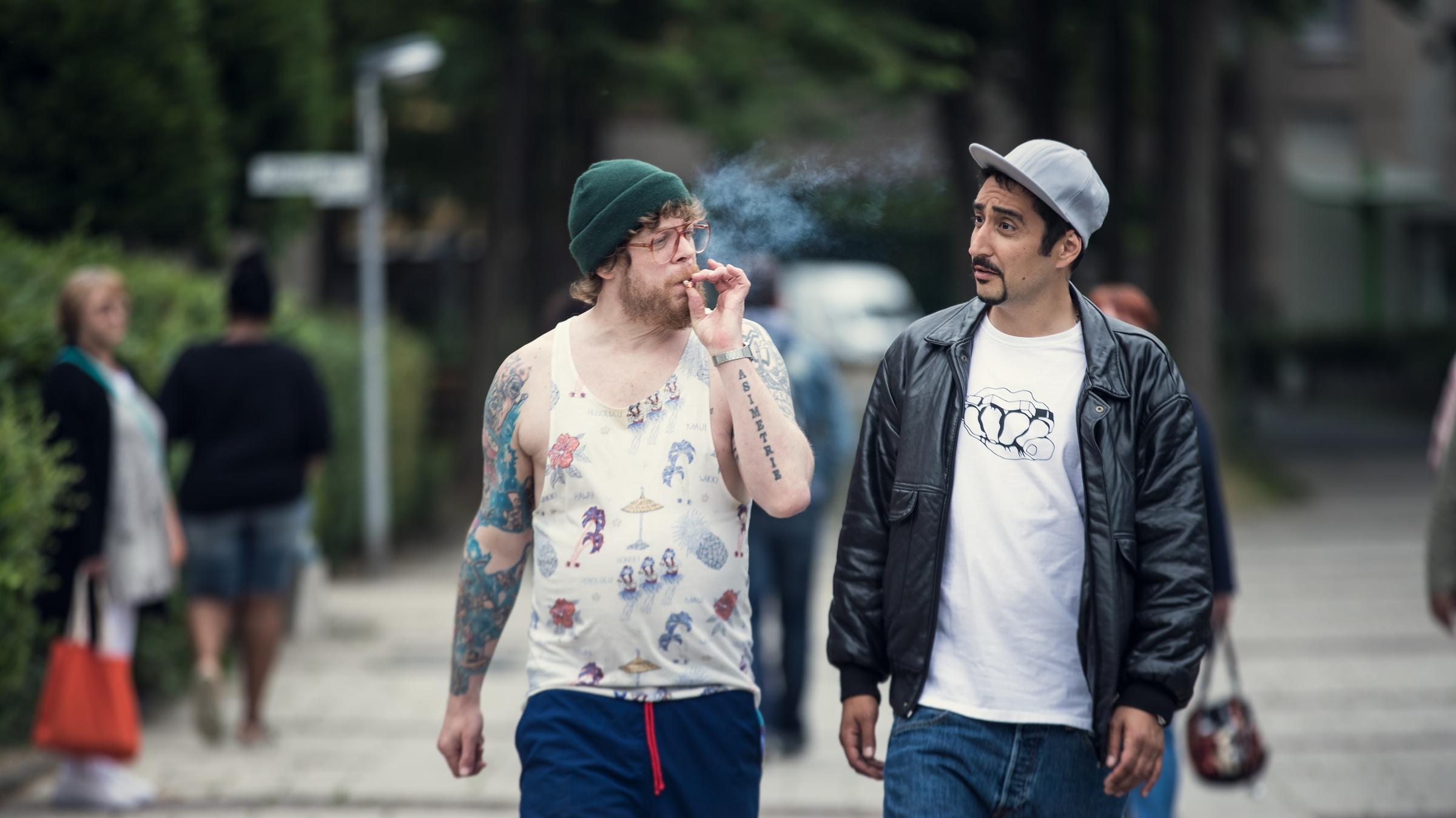 „BLOCKBUSTAZ – Comeback“: Sol (Eko Fresh) und Hardy (Sascha Reimann) laufen durch ihr Viertel. Hardy raucht.