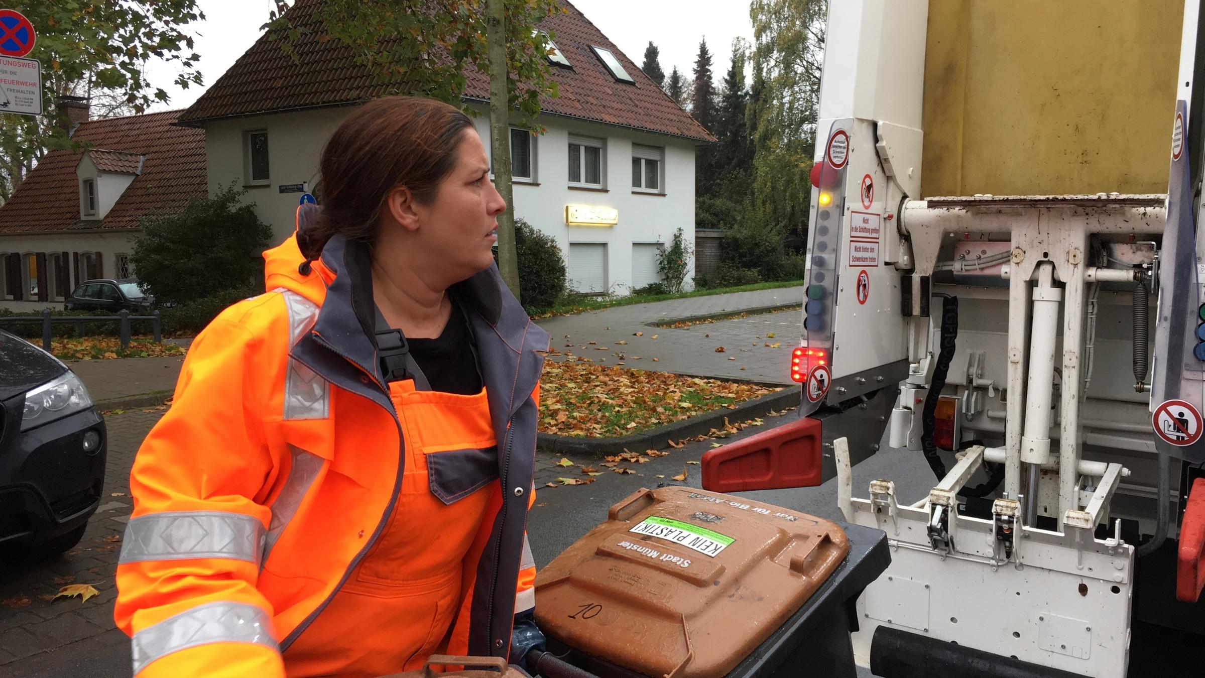 "37°: Die Dreckwegmacher - Knochenjob Müllabfuhr": Müllwerkerin Janine steht mit zwei Mülltonnen hinter dem Müllwagen auf der Straße.