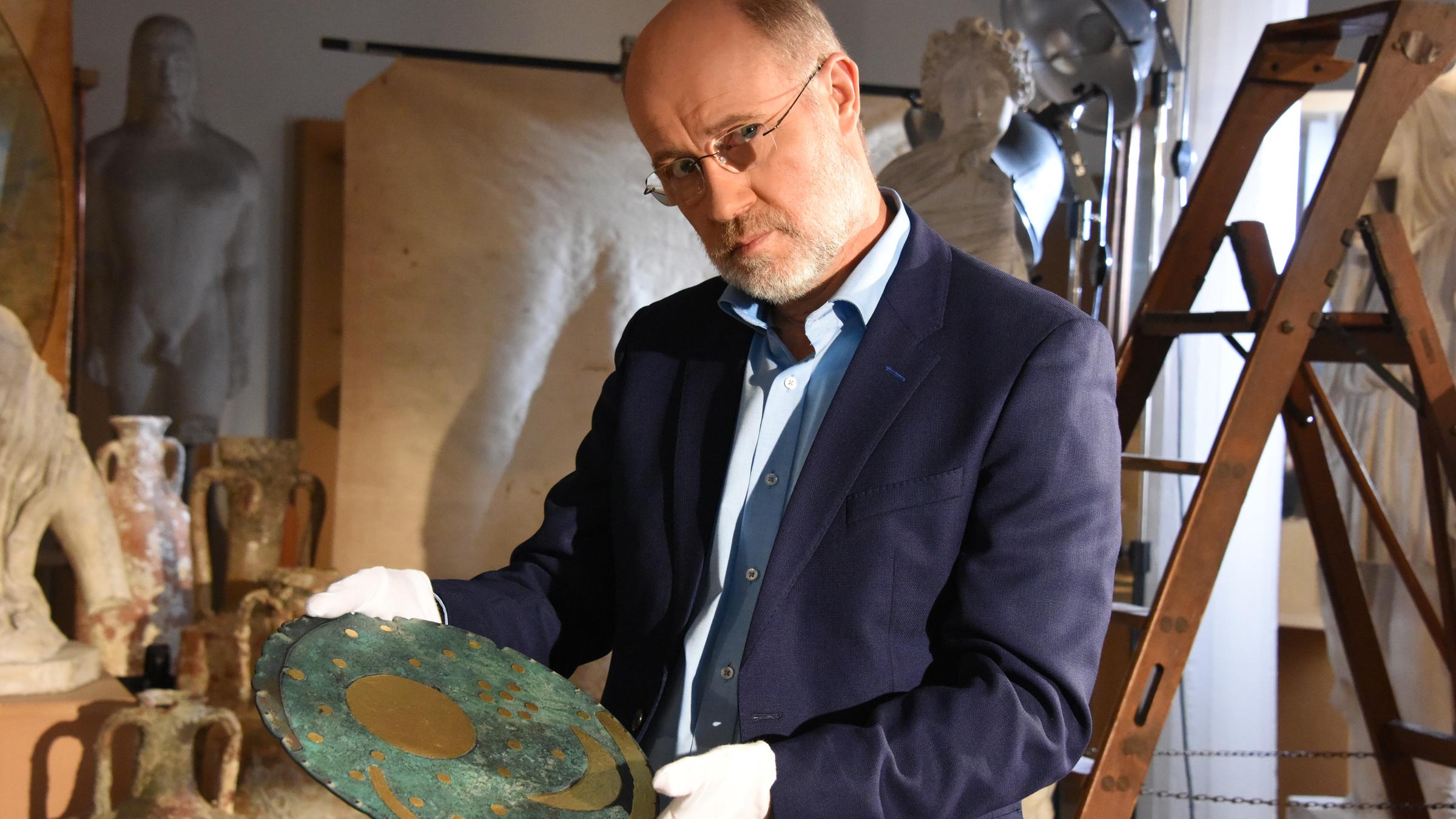 "Terra X: Ungelöste Rätsel der Archäologie: Verlorenes Wissen": Harald Lesch steht mit einer verzierten Bronzescheibe in der Hand inmitten von Requisiten.