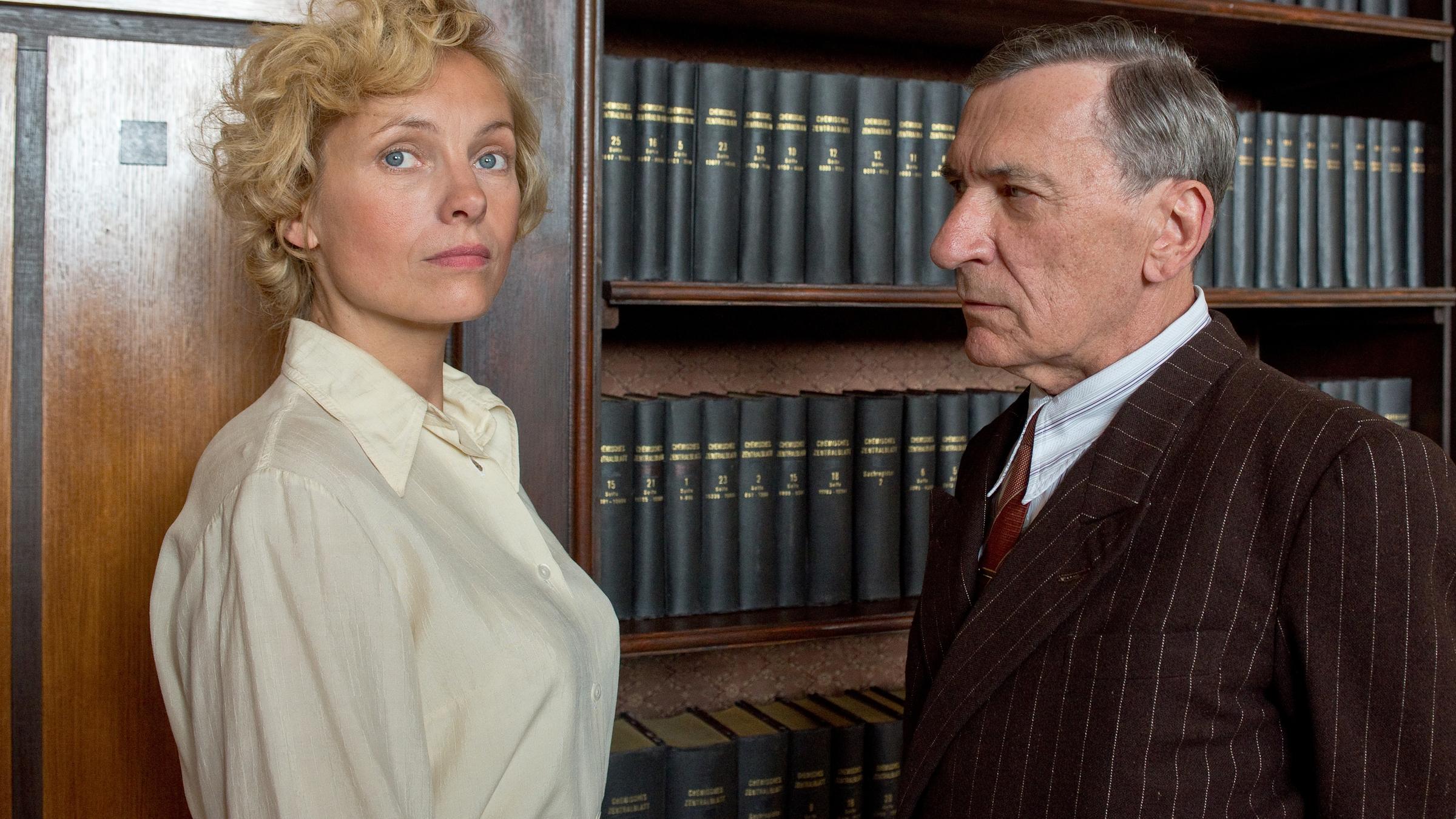 "Ich werde nicht schweigen": Margarete Oelkers ( Nadja Uhl, li) und Amtsarzt Dr. Ahrens (Rudolf Kowalski, re) stehen vor einem Bücherregal. Margarete blickt in die Ferne, Ahrens blickt sie provozierend an.