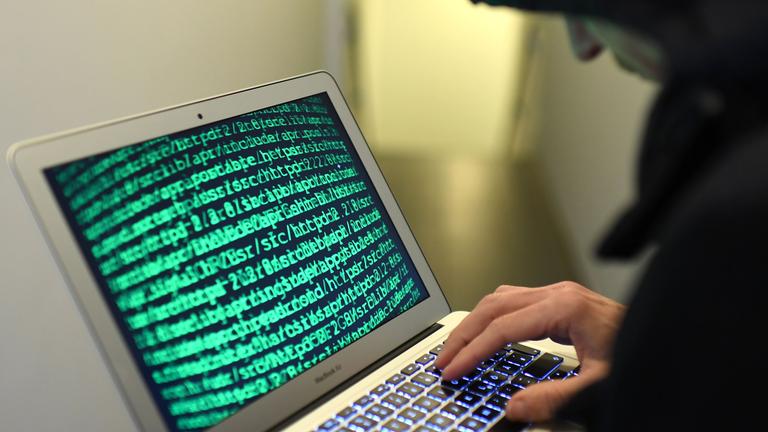 Internet und Kriminalität: Laptop grüne Schrift auf Desktop, Mann sitzt davor und tippt