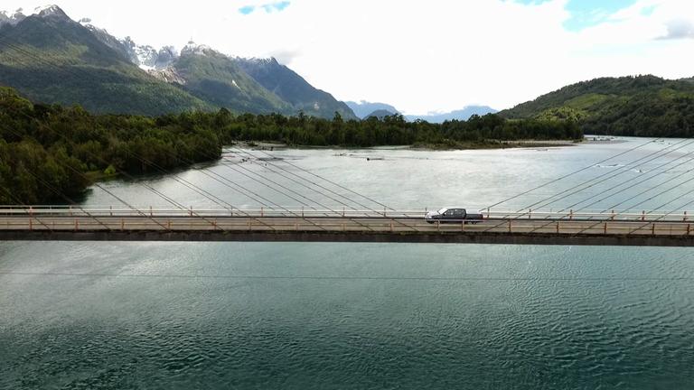 "Auf Straße 7 ins Herz von Patagonien": Auf einer Brücke über einem Fjord Patagoniens fährt ein Auto. Im Hintergrund sieht man die Landschaft Patagoniens.