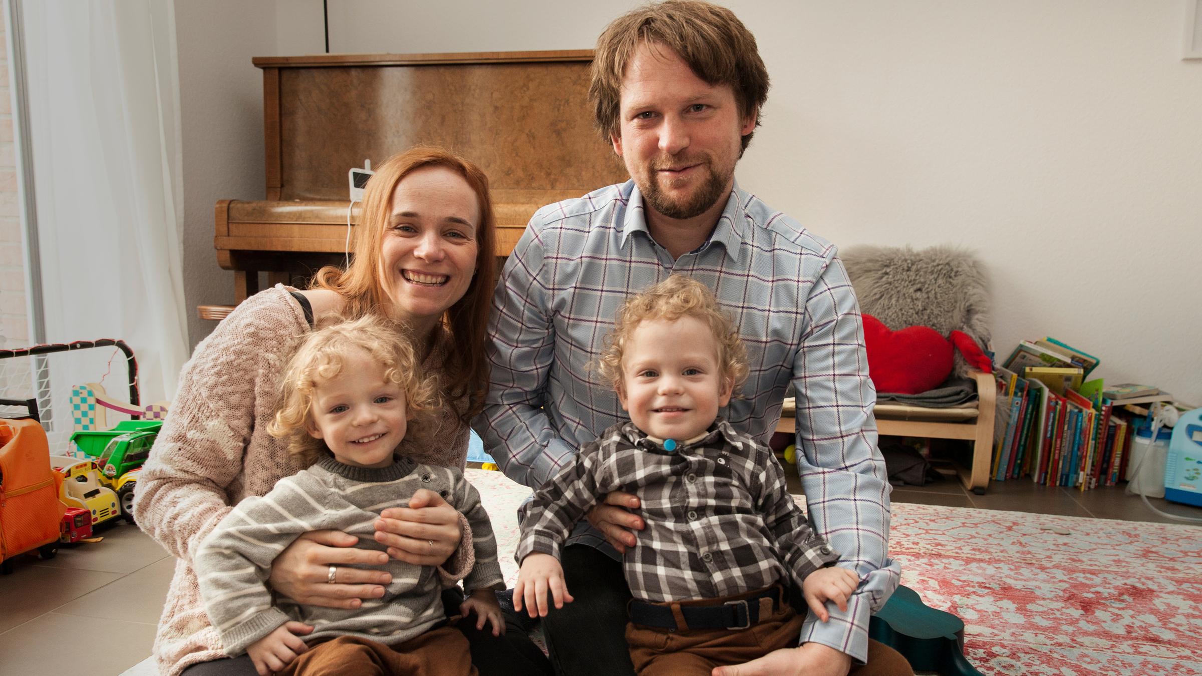 "37°: Kampf um jeden Atemzug - Wie Eltern ihr Kind retten wollen": Anja und Tony sitzen auf dem Wohnzimmerboden, Mats und Leo sitzen auf ihrem Schoß. Alle lachen in die Kamera.