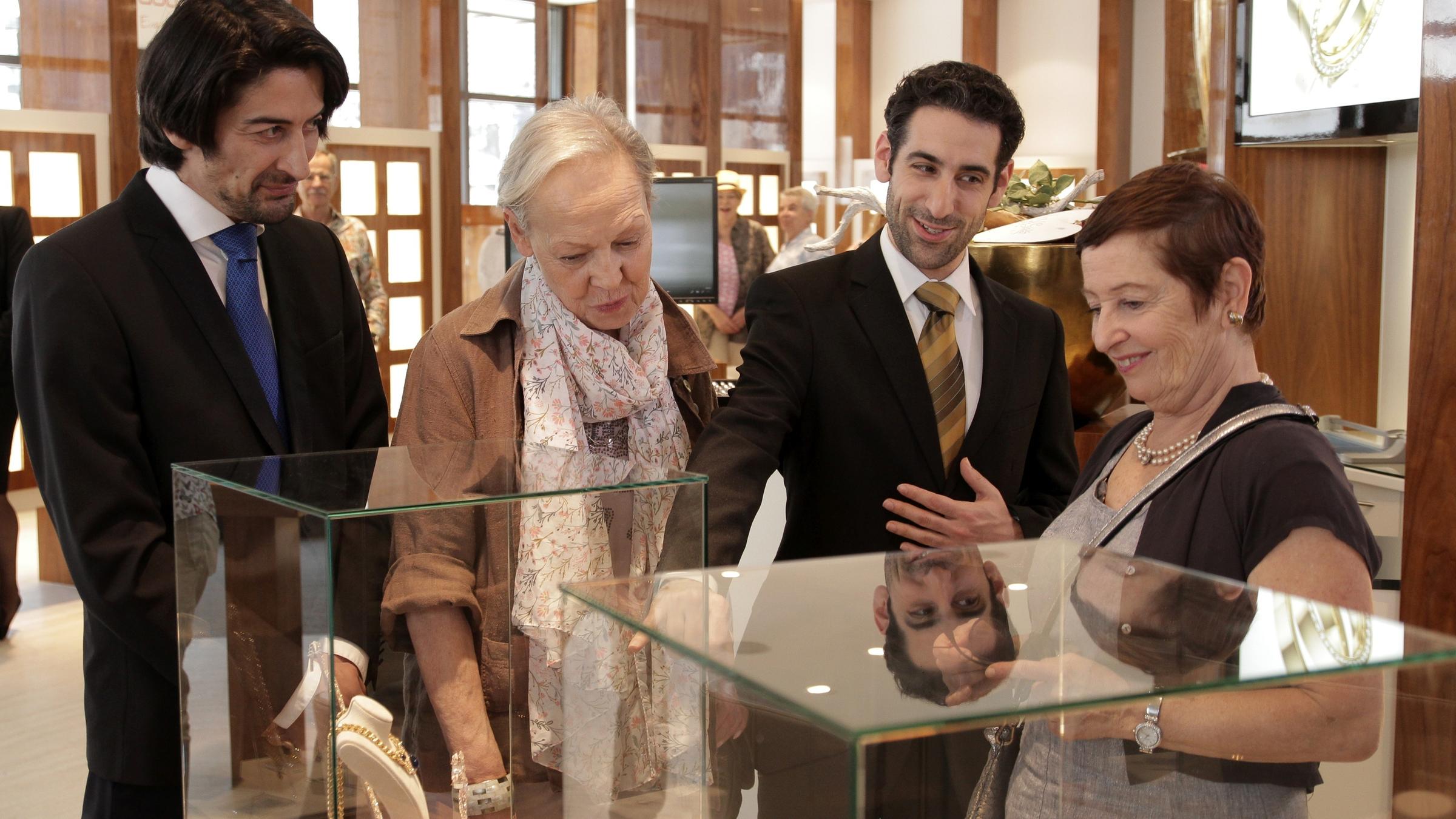 "Aktenzeichen XY-Spezial: Vorsicht, Urlaubsfalle!": Zwei ältere Damen schauen sich freudig in einem Juweliergeschäft um. Zwei Berater kümmern sich um die beiden. Im Vordergrund sieht man Glasvitrinen, in denen Schmuckstücke ausgestellt sind.