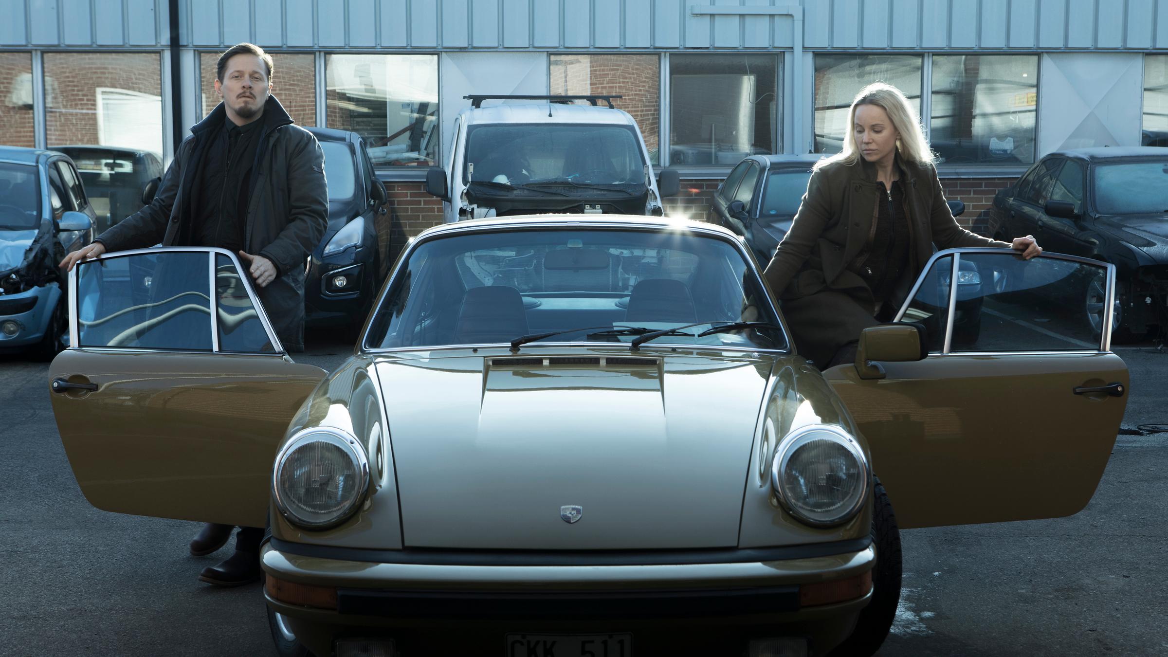 Henrik (Thure Lindhardt) steigt auf den Beifahrersitz von Sagas Oldtimer, während Saga (Sofia Helin) hinter dem Steuer Platz nimmt.