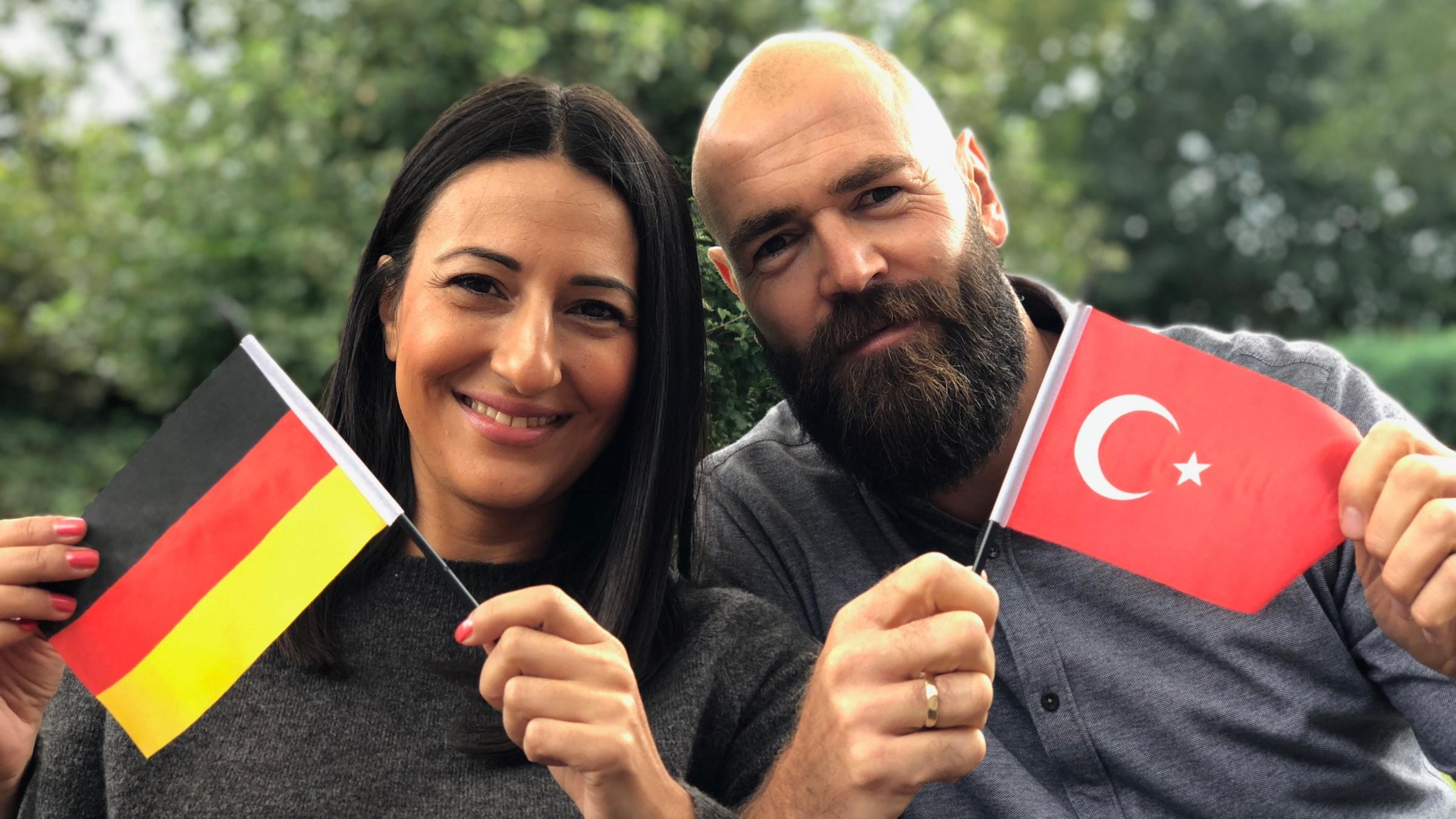 "ZDFzeit: Türken und Deutsche - Der große Nachbarschaftstest": Yasemin und Christian, ein deutsch-türkisches Ehepaar, lächelt mit der jeweiligen Nationalflagge in die Kamera.
