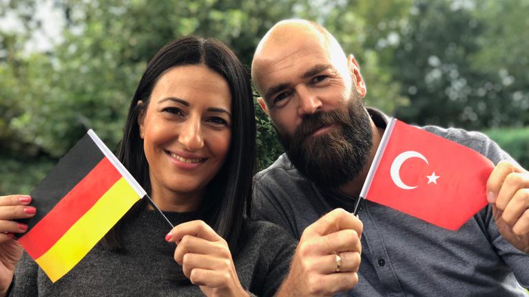 "ZDFzeit: Türken und Deutsche - Der große Nachbarschaftstest": Yasemin und Christian, ein deutsch-türkisches Ehepaar, lächelt mit der jeweiligen Nationalflagge in die Kamera.