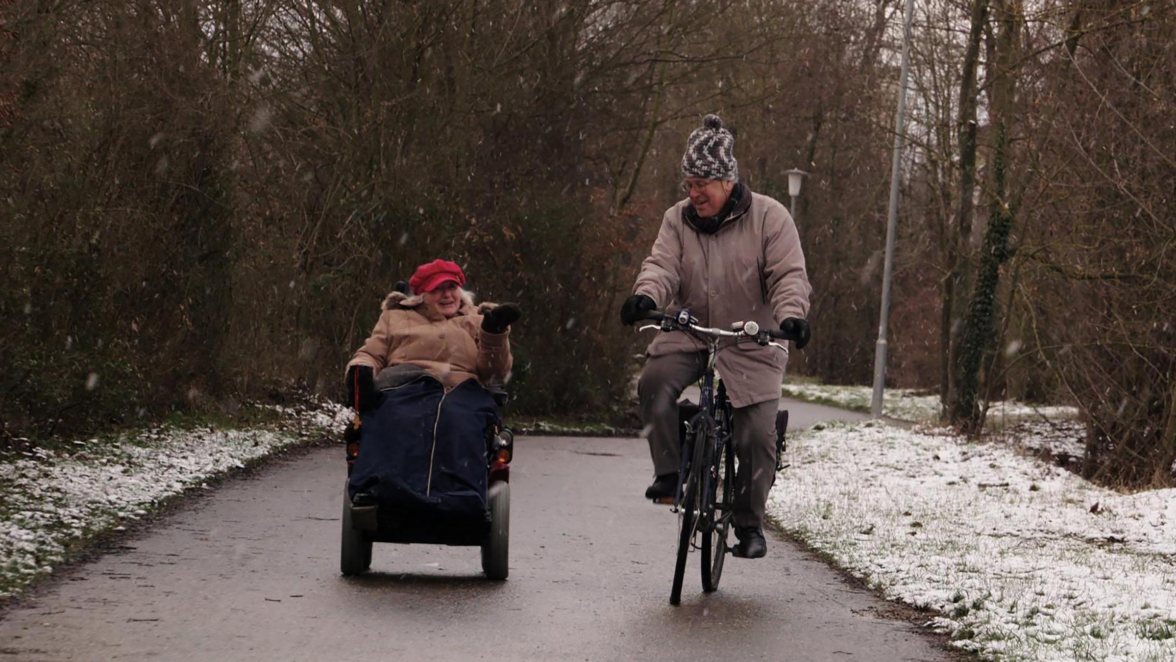 "37°: Der Rest ist Glücksache - Über Zufriedenheit im Alter": Rösli und Joachim fahren einen Weg in Sinsheim entlang. Sie ist im Rollstuhl, er fährt mit dem Fahrrad.