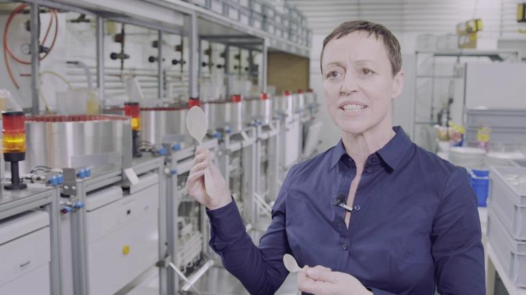 "ZDFzeit: Der große Warentest - Richtig sparen im Haushalt": Cecilia Maeusel steht im Labor und hält einen Löffel nach oben. Einen weiteren Löffel hat sie in ihrer anderen Hand.