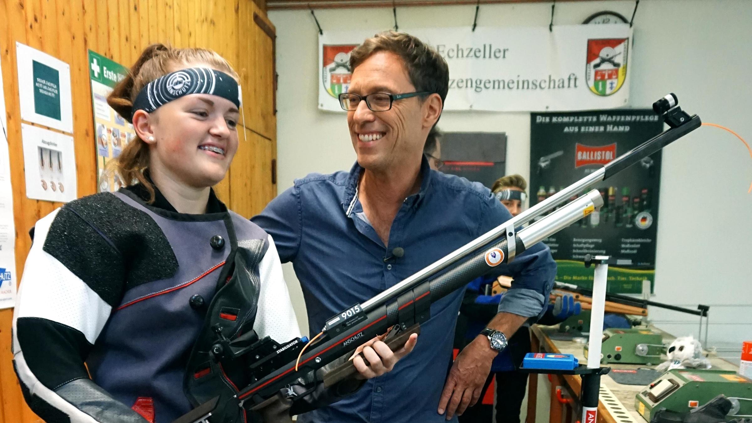 "Die neue Lust am Schießen" - Jugendliche zeigt Reporter ihr Luftgewehr. Beide lachen.