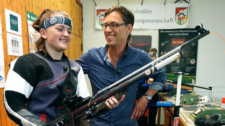 "Die neue Lust am Schießen" - Jugendliche zeigt Reporter ihr Luftgewehr. Beide lachen.