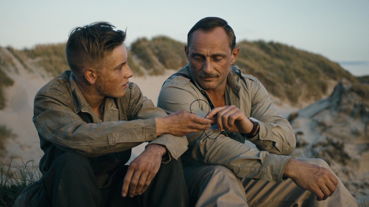 "Unter dem Sand - Das Versprechen der Freiheit": Sebastian Schumann (Louis Hofmann) und Unteroffizier Carl Rasmussen (Roland Møller) sitzen nebeneinander in den Dünen.