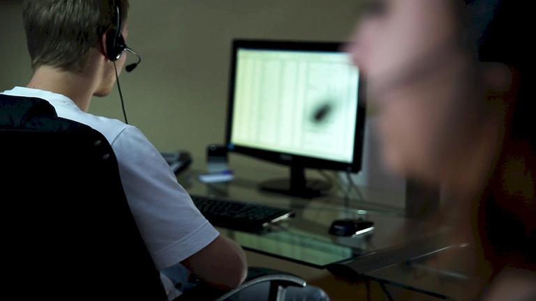 "ZDFzoom: Bei Anruf Abzocke - Betrug aus dem Callcenter": Ein junger Mann sitzt vor seinem Monitor und telefoniert dabei.