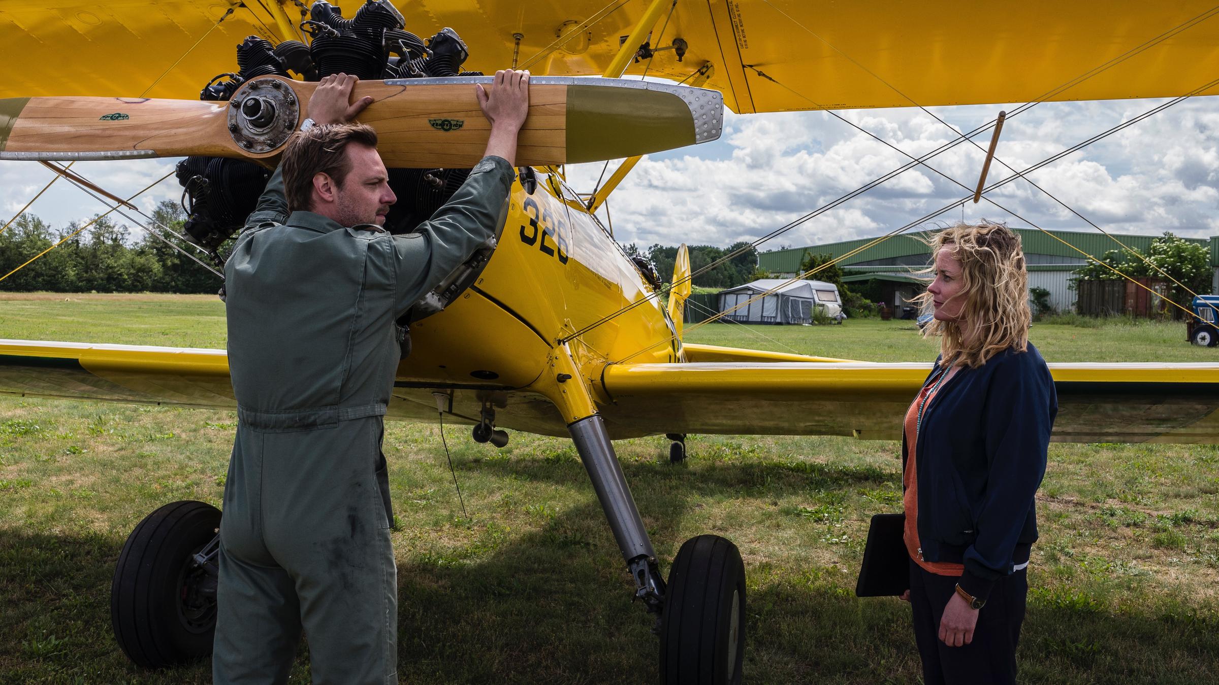 "Lotte Jäger und die Tote im Dorf": Auf dem ländlichen Landeplatz steht Florian Grasso (Christoph Letkowski) die Hände am Propeller seines Doppeldeckers, neben Lotte Jäger (Silke Bodenbender) und schaut sie an.