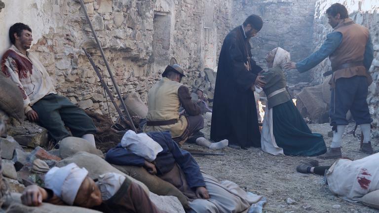  "Terra X - Der Dreißigjährige Krieg - Tagebücher des Überlebens": Verletzte und erschöpfte Menschen (Darsteller) in einer Gasse. Im Hintergrund kniet eine Frau vor einem Mann und scheint ihn anzuflehen. Hinter ihr steht ein weiterer Mann und greift nach ihrer Schulter.