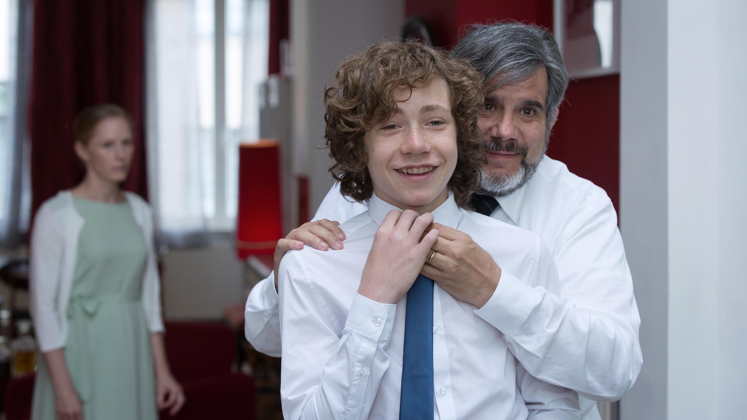 "Der Tod und das Mädchen - Van Leeuwens dritter Fall": Piet Martens (Bruno Cathomas) hilft Nils Martens (Mats Thiersch beim Krawattebinden. Fleur Martens (Susanne Wuest) steht hinter ihnen im Raum.