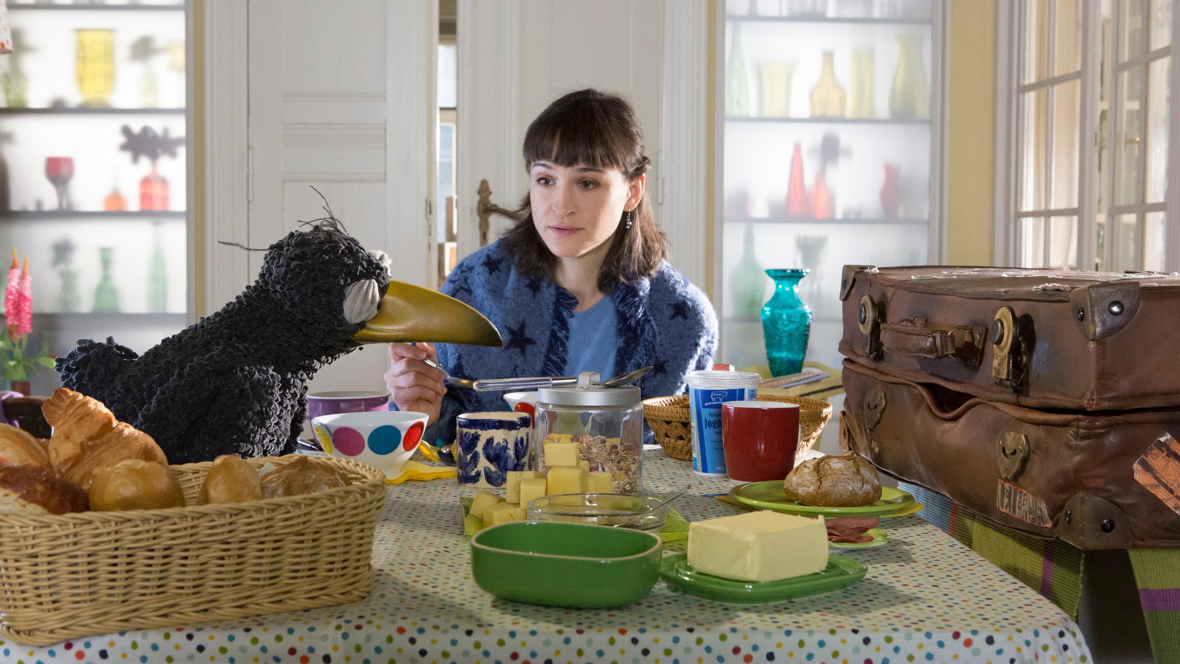 Siebenstein - "Ein Zimmer für mich allein": Rabe Rudi (Werner Knoedgen) und der Koffer (Thomas Rohloff) hocken streitend am Küchentisch gegenüber. Zwischen ihnen sitzt eine ratlose Siebenstein (Henriette Heinze).