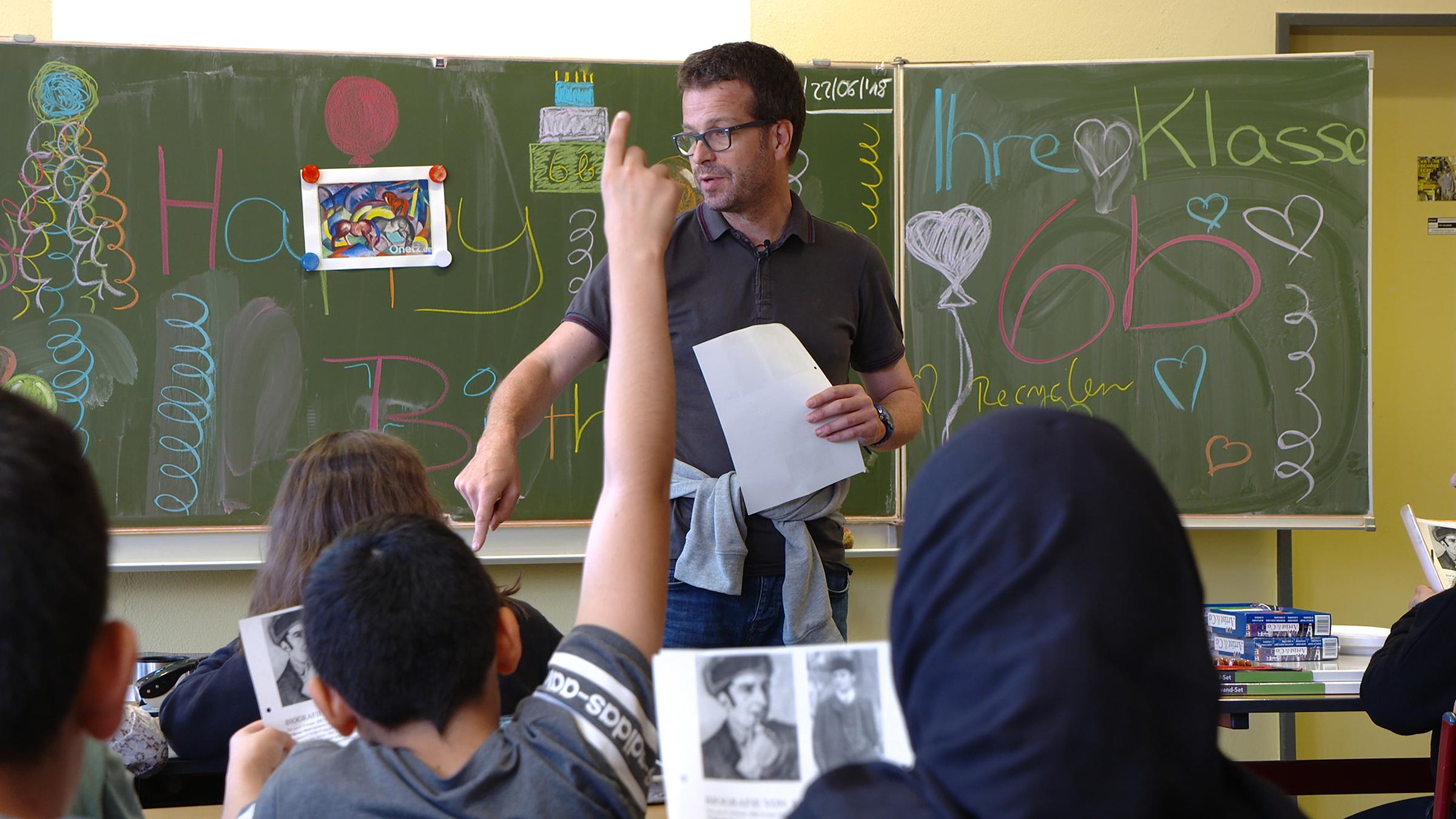 "37°: Lehrer am Limit - Dauerstress im Schulalltag": Christof B. steht vor einer Tafel im Klassenraum. Im Vordergrund melden sich Schüler.