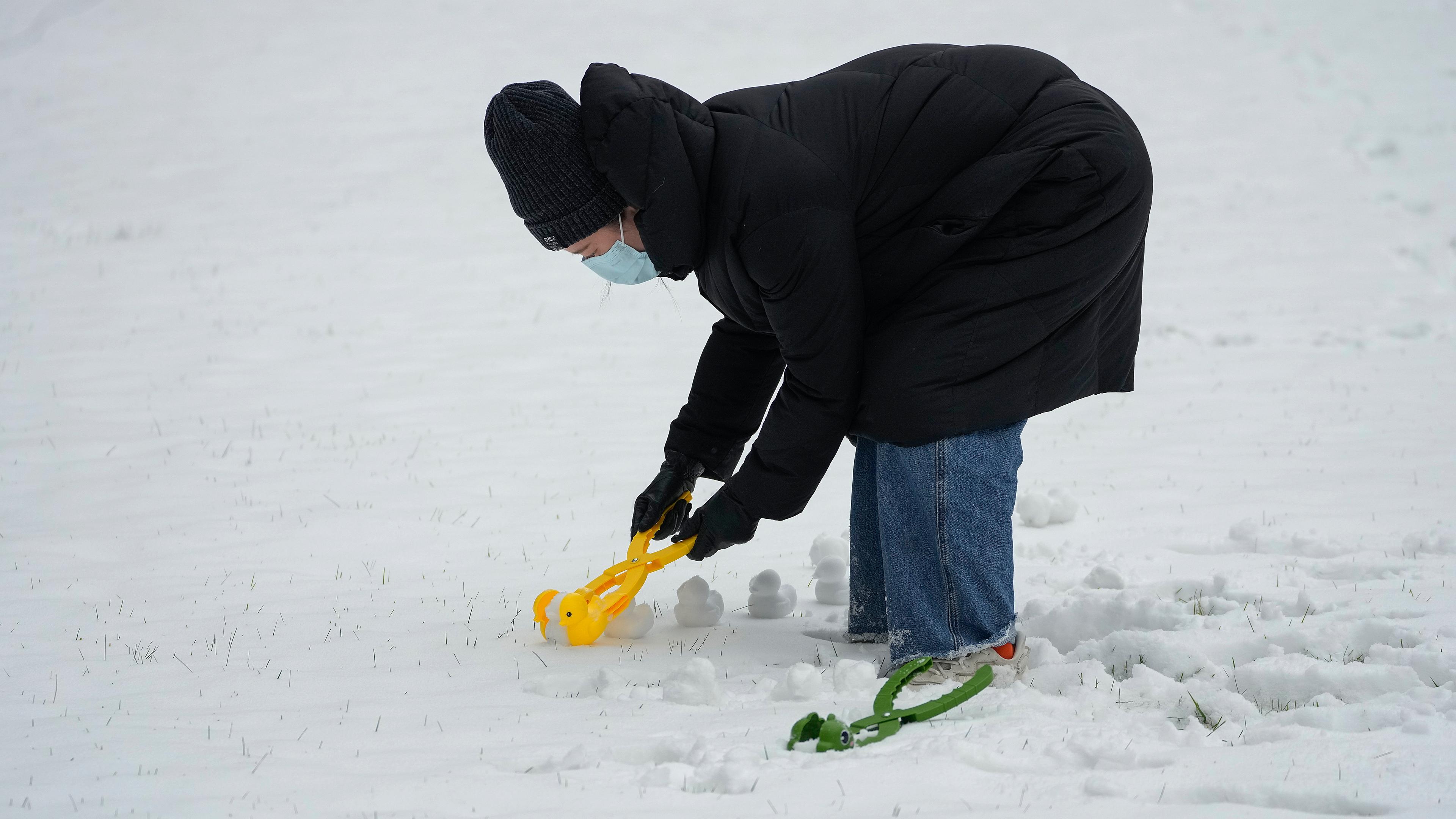Eine steht im Schnee und bückt sich herab. In ihrer Hand hält sie ein Spielzeug, eine Art Zange, gelb und aus Plastik, mit der sie Schneebälle zu Quietscheentchen formt. Neben ihr im Schnee liegt ein zweites Zangenspielzeug, grün und in Form eines Drachen.
