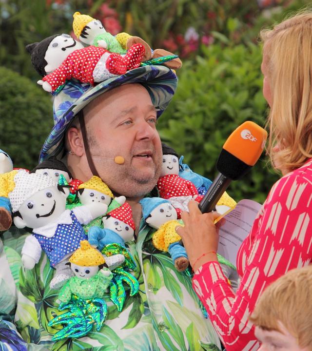 "ZDF-Fernsehgarten": Dirk Bach 2011 im Gespräch mit Andrea Kiewel. Er trägt ein Kostüm und einen Hut aus lauter Stoff-Mainzelmännchen.
