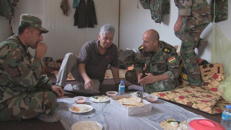 "An vorderster Front - Der Krieg gegen den IS": Ashwin Raman beim Essen mit Oberst Leutnant Hiwa Amin und einem weiteren Soldaten. Sie essen auf dem Boden.