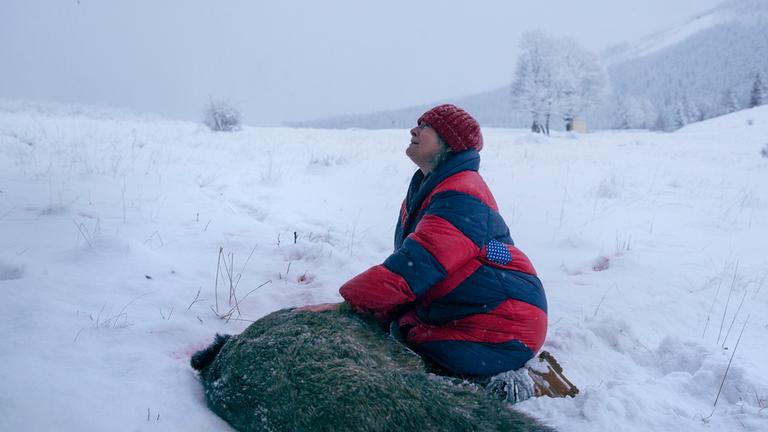 "Pokot" (ARTE): Janina Duszejko (Agnieszka Mandat) kniet in einer verschneiten Landschaft mit schmerzendem Gesichtsausdruck  neben einem toten Wildschwein