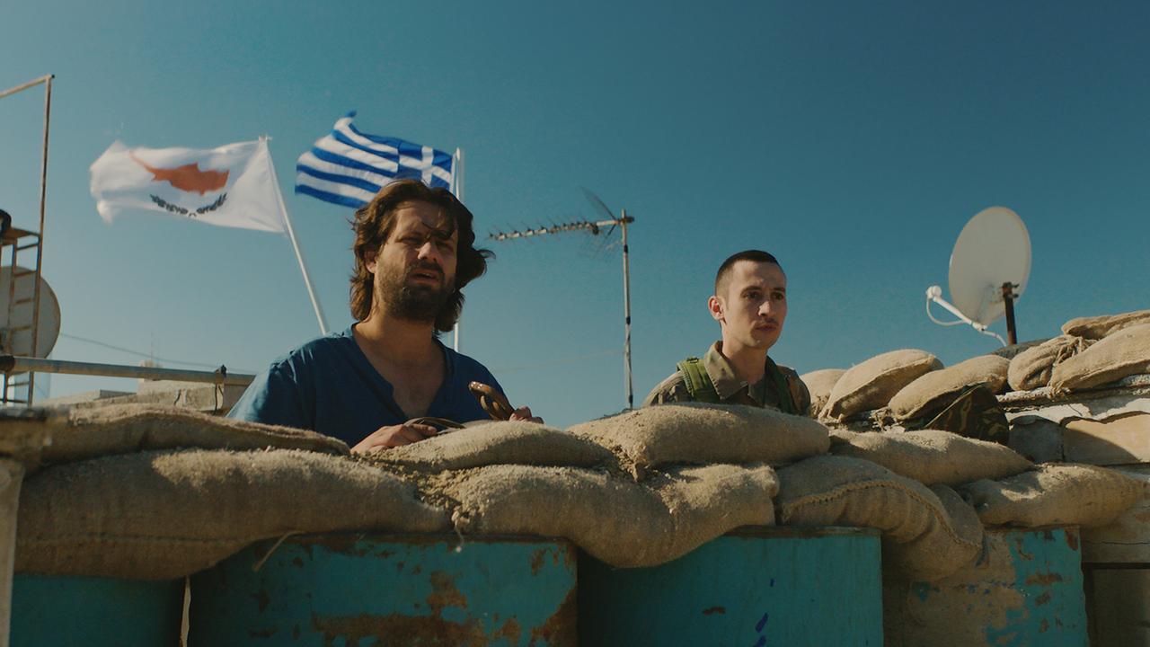 „Smuggling Hendrix“: Yiannis (Adam Bousdoukos,l.) steht neben Grenzsoldat hinter Sandsäcken.