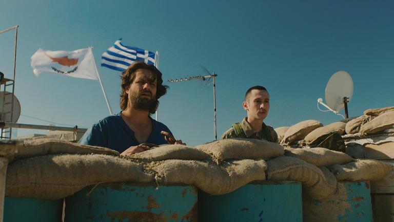 „Smuggling Hendrix“: Yiannis (Adam Bousdoukos,l.) steht neben Grenzsoldat hinter Sandsäcken.