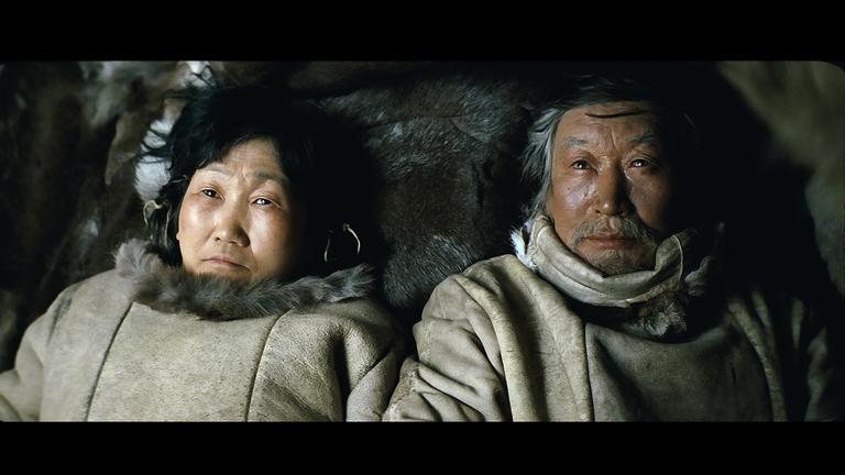 "Ága":  Eine Inuit-Frau und ein Inuit-Mann liegen nebeneinander auf einem Fell und schauen in die Kamera