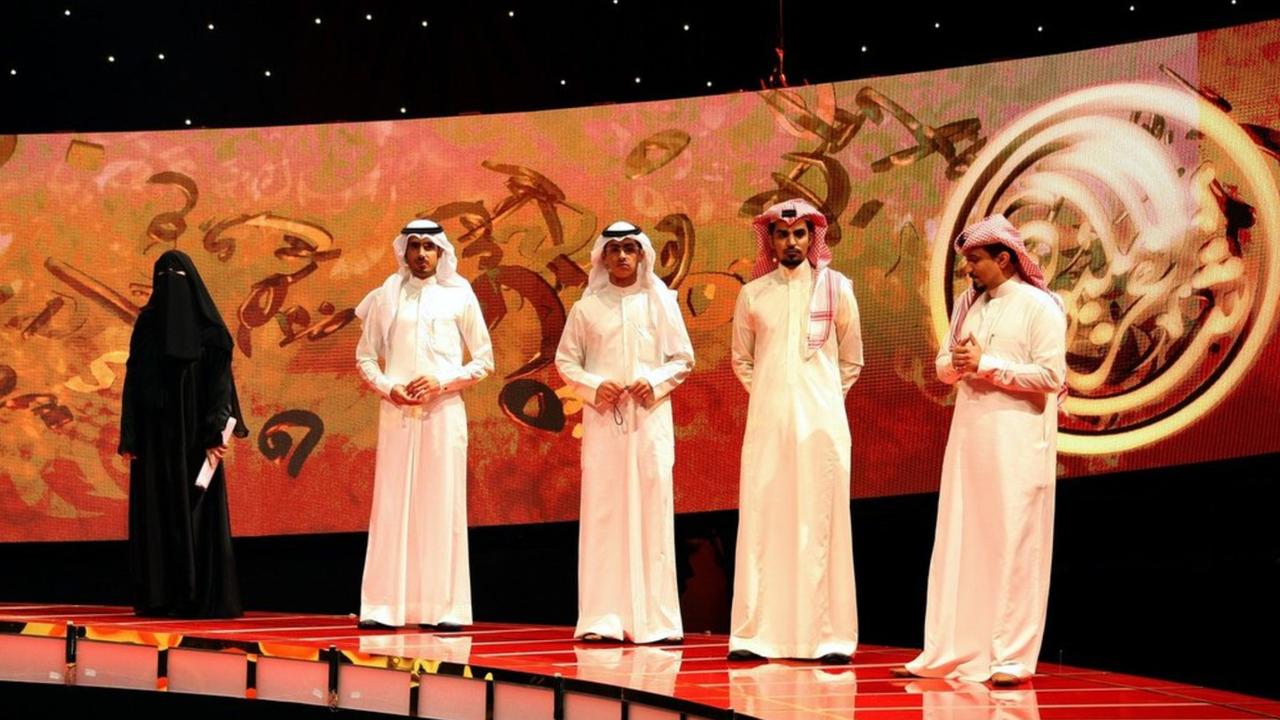 "Hissa Hilal - eine Stimme hinter dem Schleier": Hissa Hila trägt einen schwarzen Nikab und steht mit vier weiß gekleideten Männern im TV-Studio.