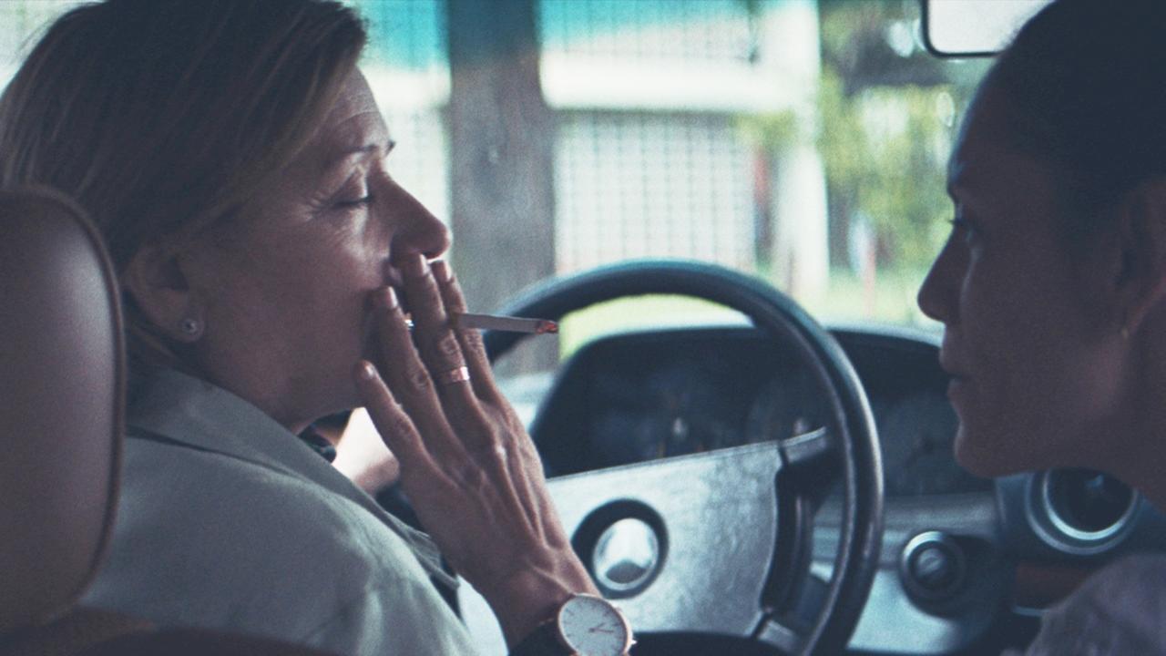 Chela (Ana Brun) sitzt rauchend am Steuer eines Autos und schaut dabei Angy (Ana Ivanova) auf dem Beifahrersitz an.